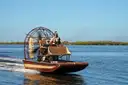 An airboat speeding across open water with mangroves on the horizon
