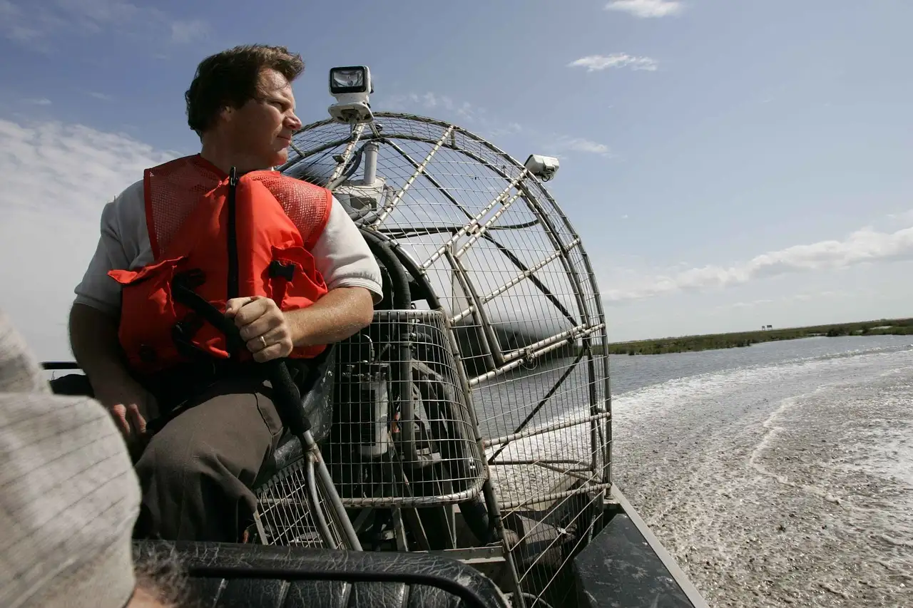 An airboat pilot at the controls with the fan cage behind him