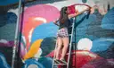 An artist on a ladder spray-painting a colourful mural