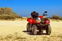 A red ATV parked on sand under a blue sky