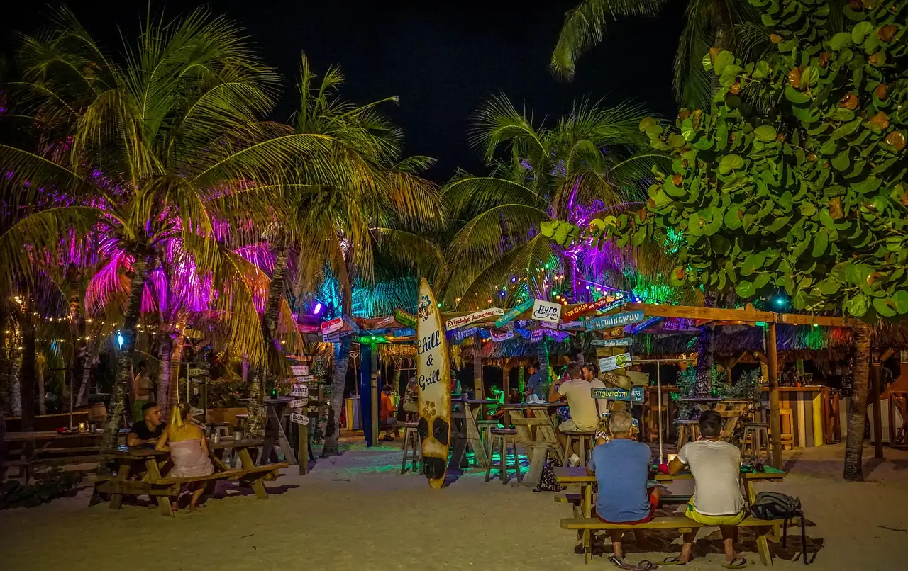 A palm-lined beach bar lit up in blue and pink at night