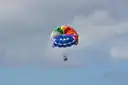 A rainbow-coloured parasail in a cloudy sky