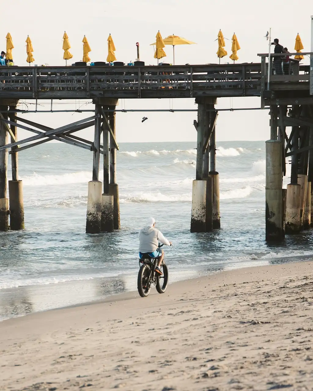 A cyclist riding along the sand beside a pier