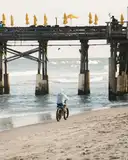 A cyclist riding along the sand beside a pier