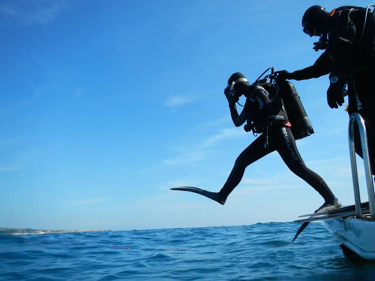 Divers stepping off the back of a dive boat into the sea