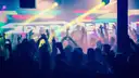 A club crowd with raised hands under coloured stage lights