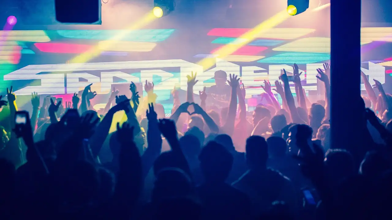A club crowd with raised hands under coloured stage lights
