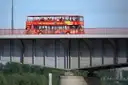 An open-top double-decker sightseeing bus crossing a bridge
