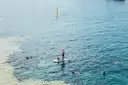 A paddleboarder standing among snorkelers in clear blue water, seen from above