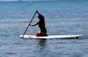 A paddleboarder kneeling on a white board on blue water