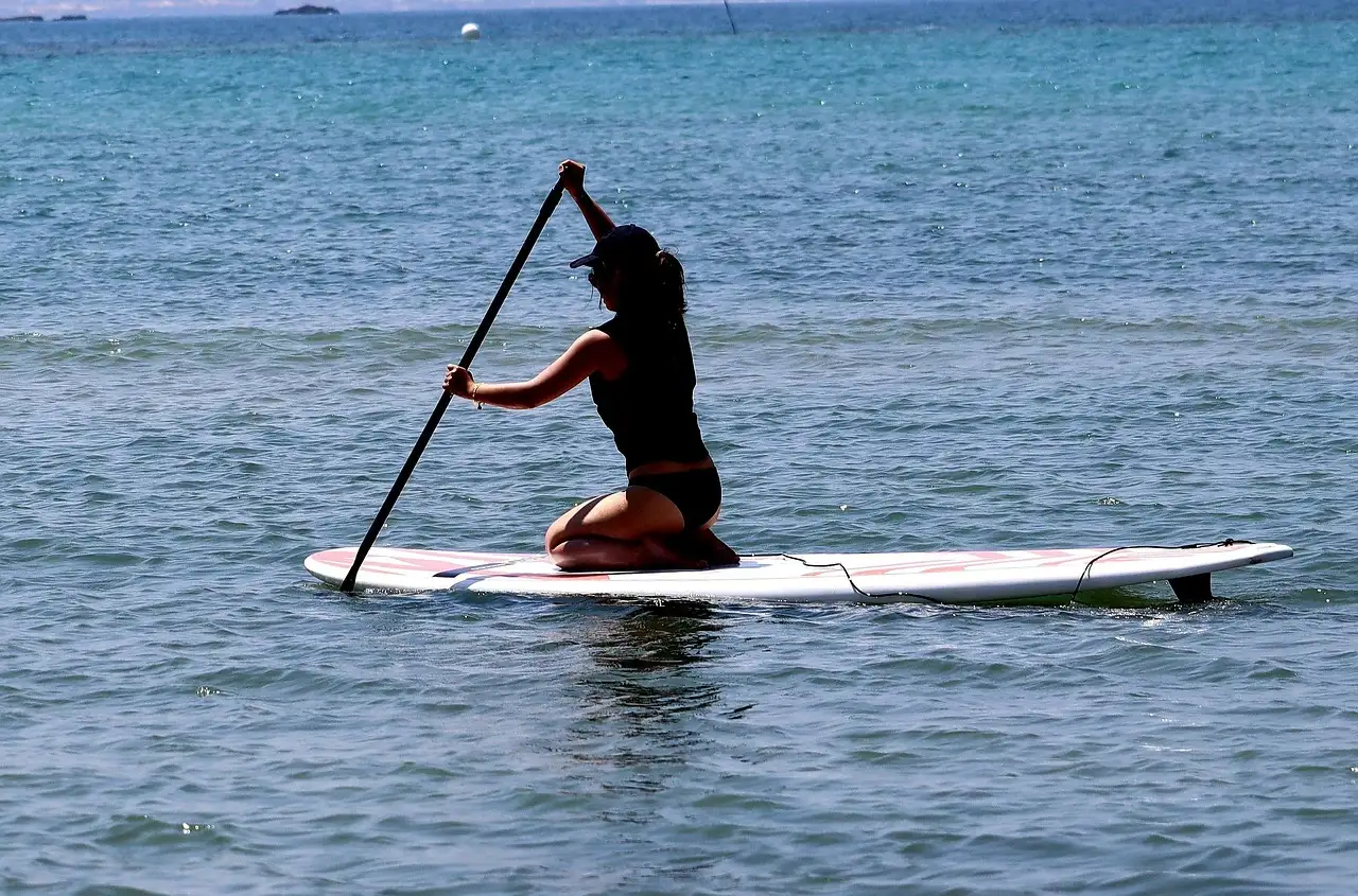 A paddleboarder kneeling on a white board on blue water