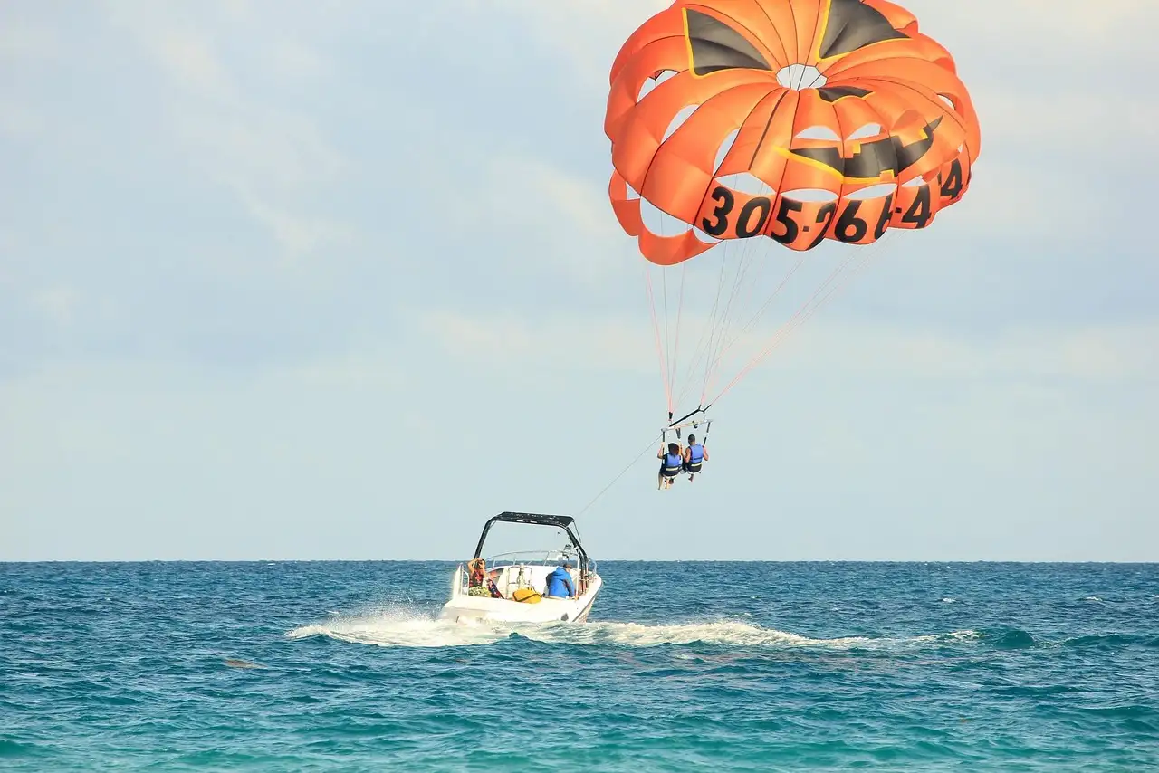 Two riders under an orange parasail, towed by a boat off Miami