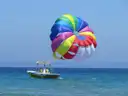 A rainbow parasail flying above its tow boat on blue sea