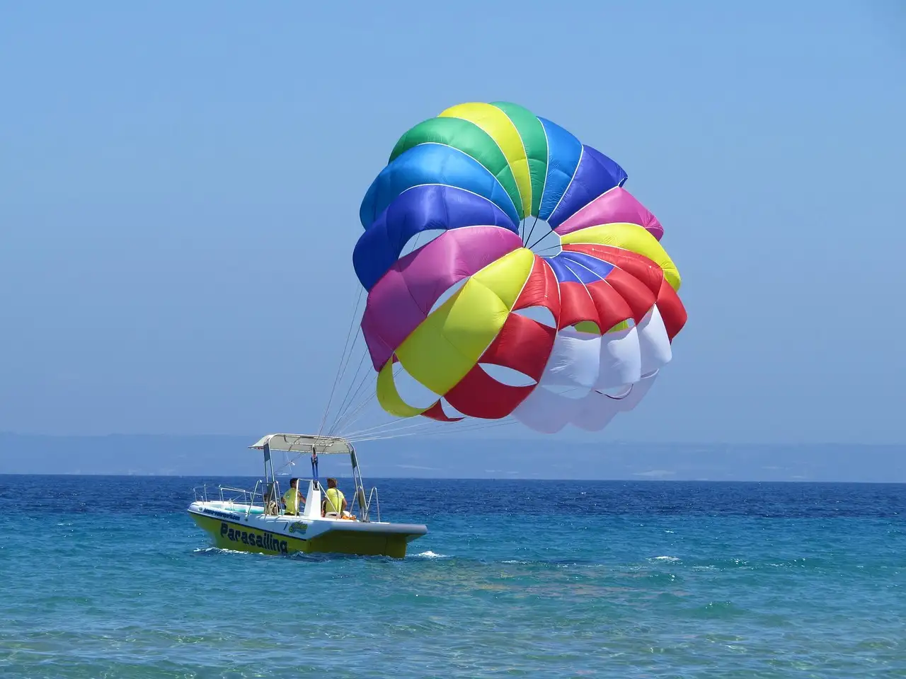 A rainbow parasail flying above its tow boat on blue sea