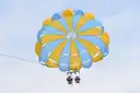 Two riders side by side under a blue and yellow parasail