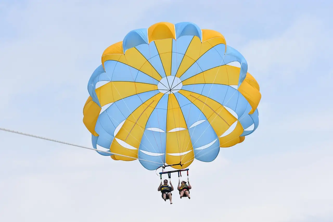 Two riders side by side under a blue and yellow parasail