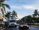 Miami Beach street lined with palm trees and parked and passing vehicles at sunrise