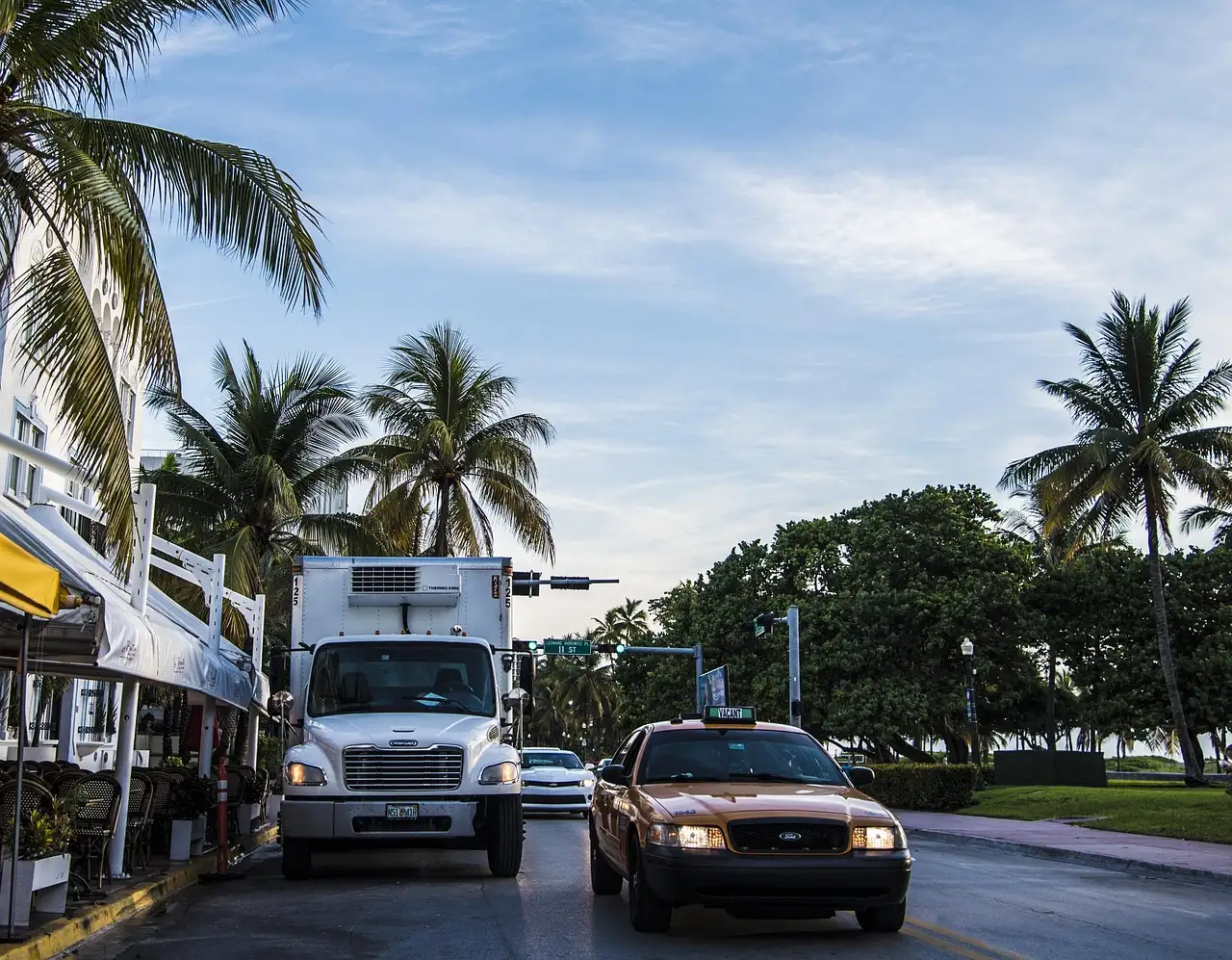 Miami Beach street lined with palm trees and parked and passing vehicles at sunrise