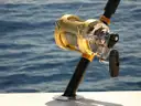 A big-game fishing rod and reel in a holder on a boat rail over blue sea