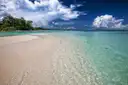 A sandbar in clear shallow water beside a green island