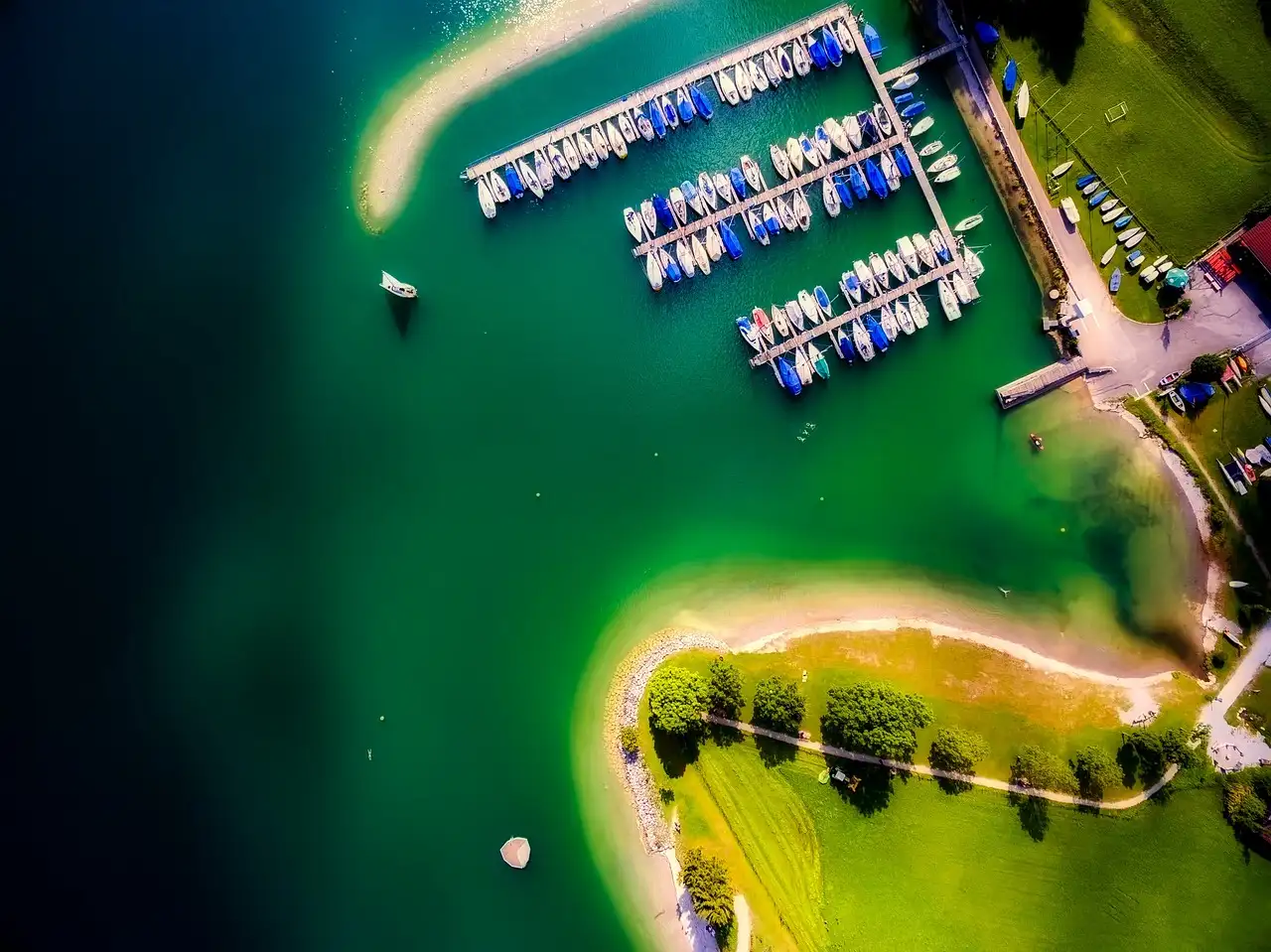 An aerial view of shallow turquoise water, green islands and a marina full of boats