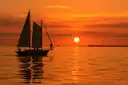 A schooner under sail against an orange sunset