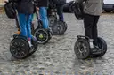 Several Segways and their riders' legs on a paved street