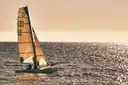 A small sailing catamaran in golden light