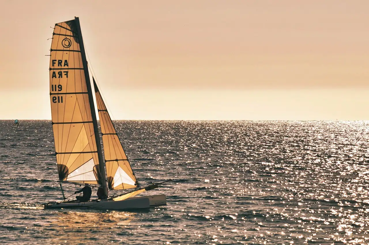 A small sailing catamaran in golden light