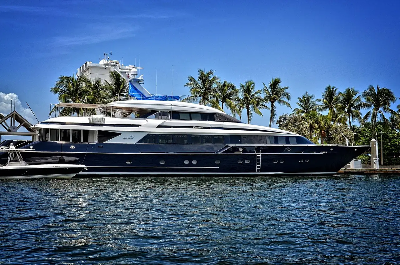 A dark-hulled superyacht moored in a palm-lined canal