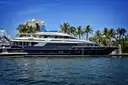 A dark-hulled superyacht moored in a palm-lined canal