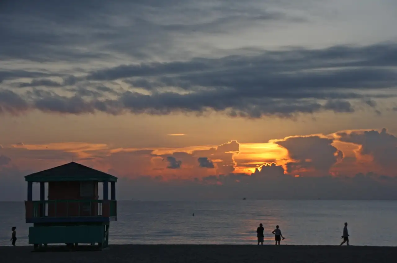 Couples walking on Miami Beach at sunset beside a lifeguard tower